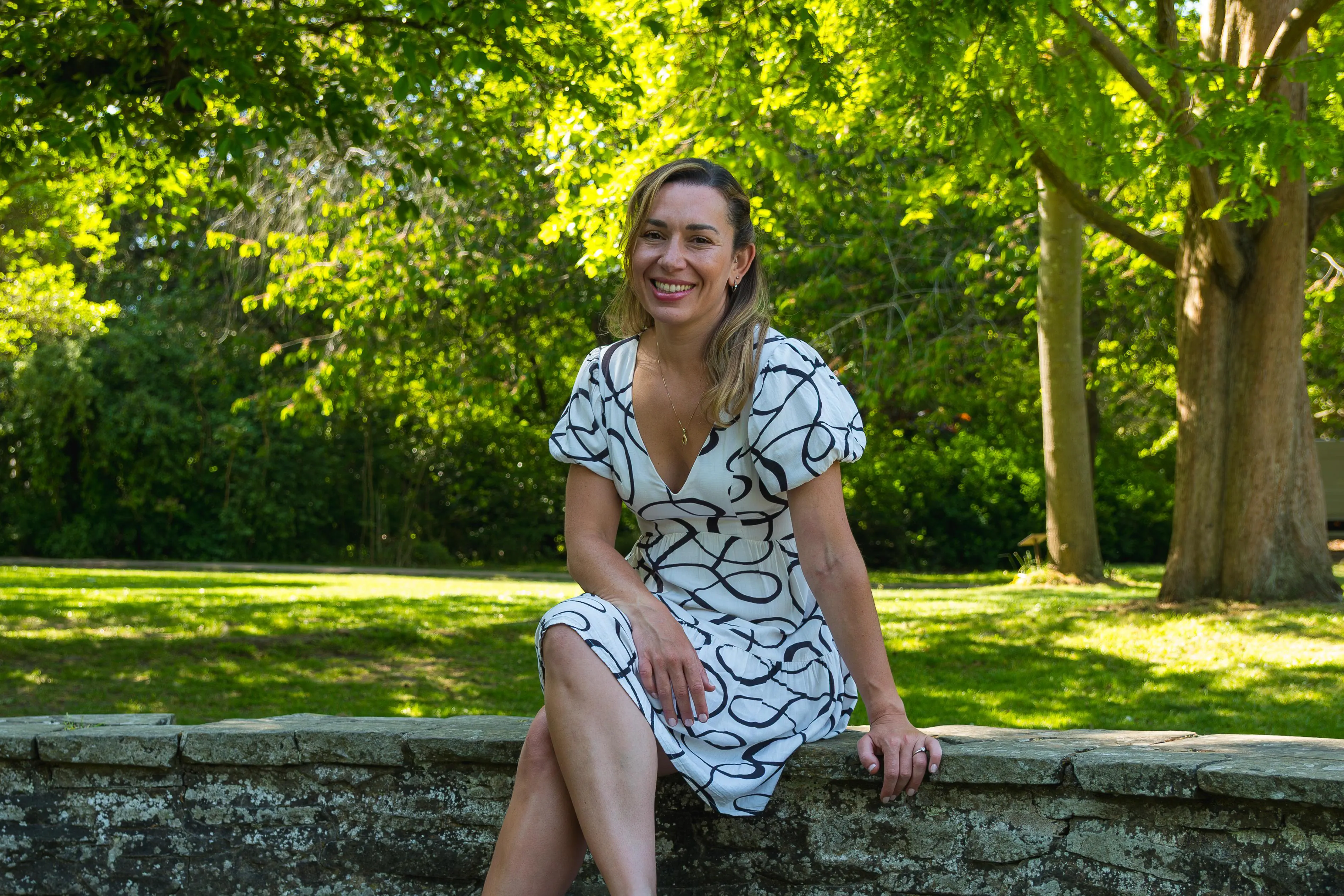 A professional female business woman smiles and sits on a stone wall